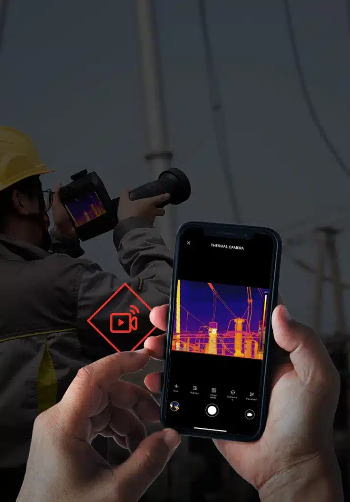 Technicien utilisant une caméra thermique tandis qu'un smartphone affiche l'image thermique d'installations électriques