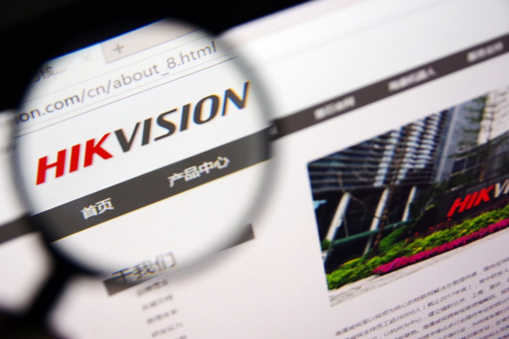 Gros plan à travers une loupe sur le logo Hikvision affiché sur un site web avec du texte en chinois.