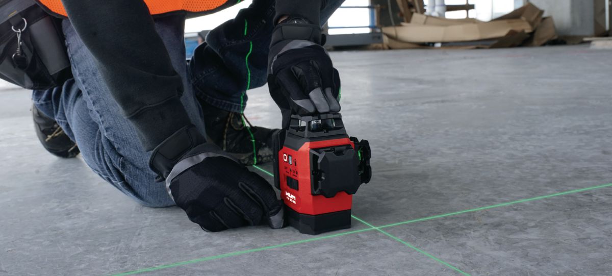 Opérateur positionnant un laser Hilti PM 30-MG sur un sol de chantier avec lignes vertes projetées