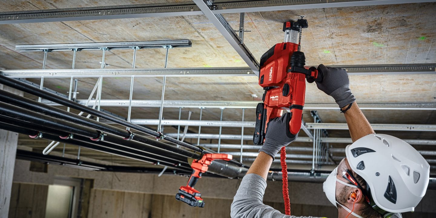 Opérateur équipé de protections utilisant un perforateur Hilti Nuron au plafond près de chemins de câbles