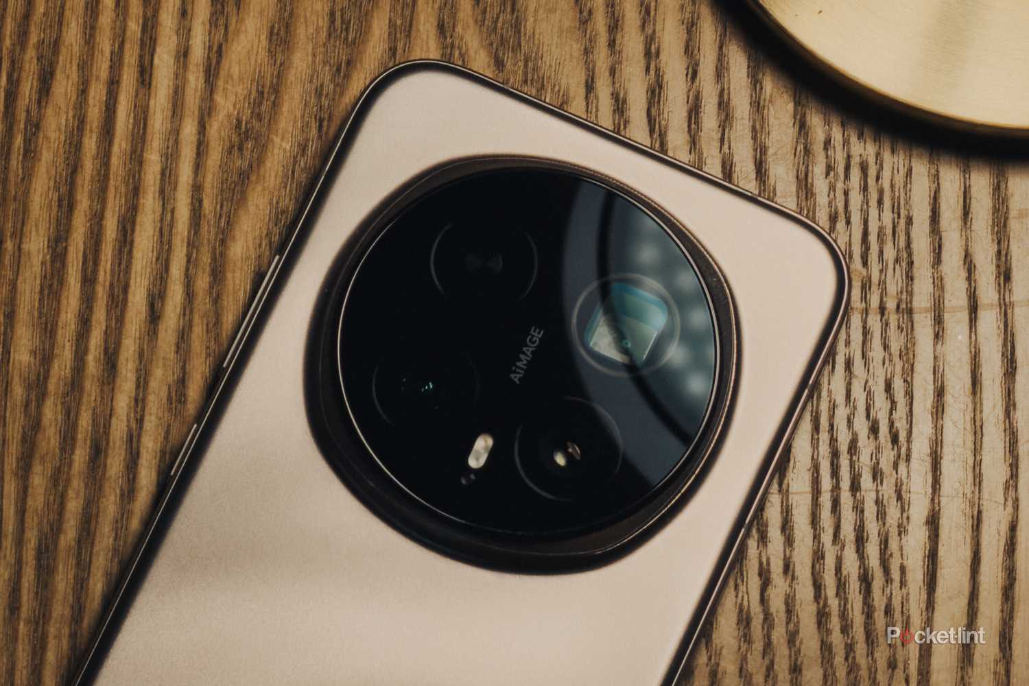 Gros plan sur le module photo circulaire d’un smartphone beige avec l’inscription AiMAGE, posé sur une surface en bois.