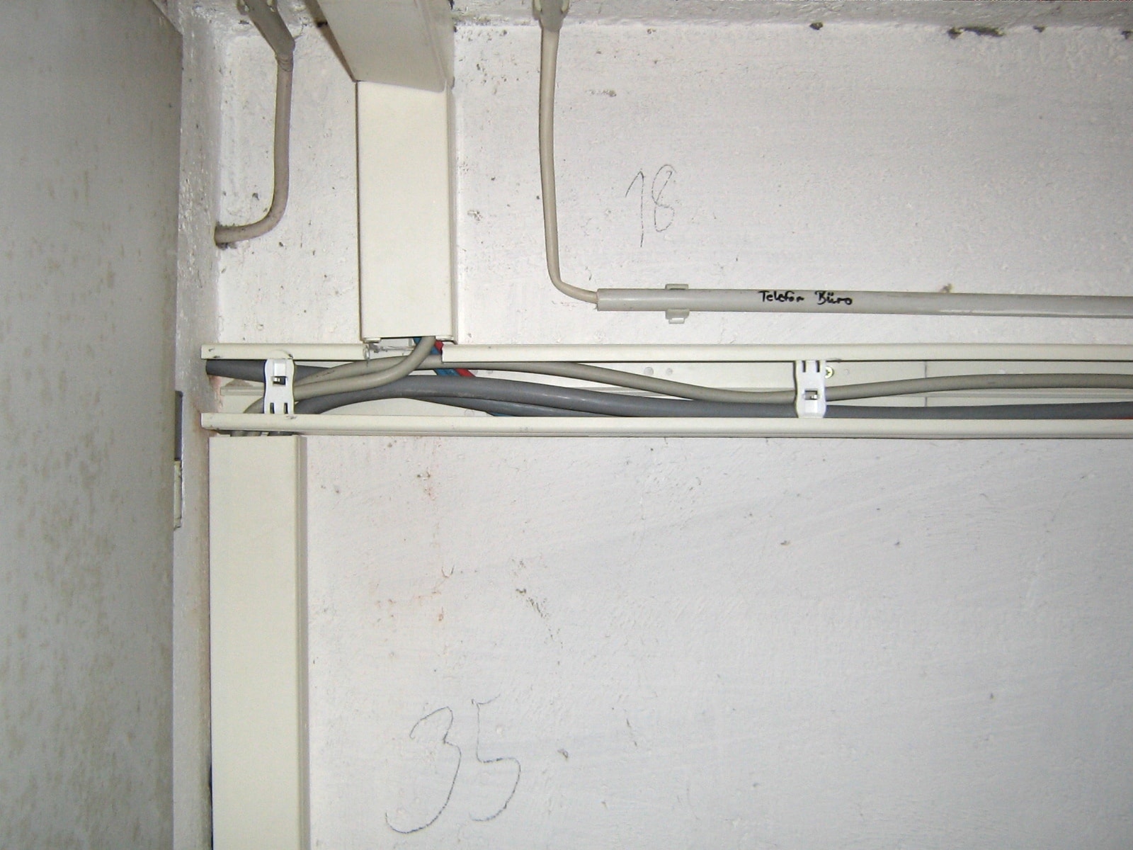 Goulotte électrique ouverte fixée à un mur, avec plusieurs câbles gris visibles à l’intérieur