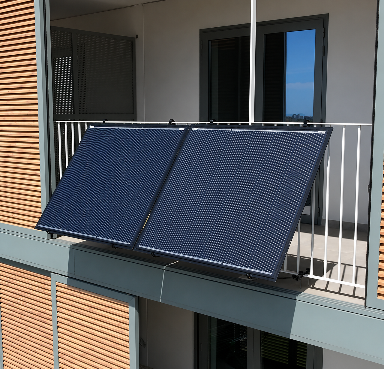 Deux panneaux solaires bleus inclinés installés sur la rambarde blanche d’un balcon d’immeuble.
