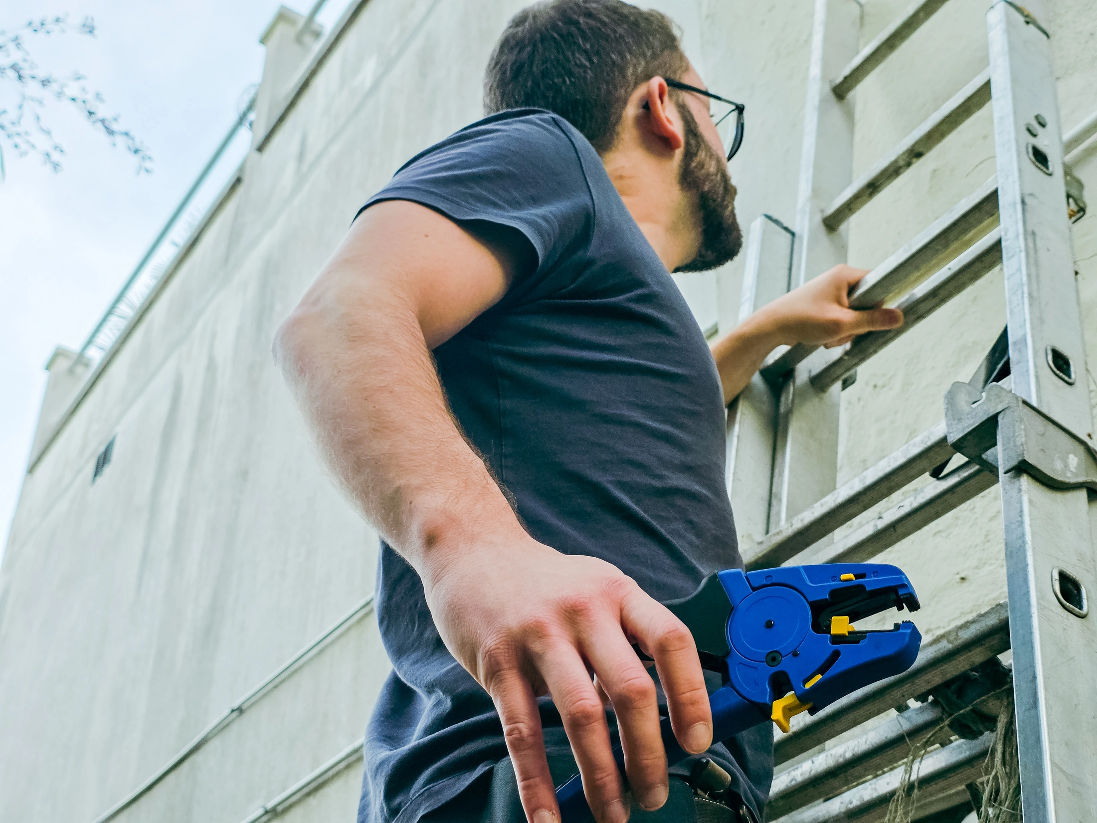 Électricien avec une pince à dénuder automatique Klauke K43/3 bleue et jaune près d'une échelle aluminium