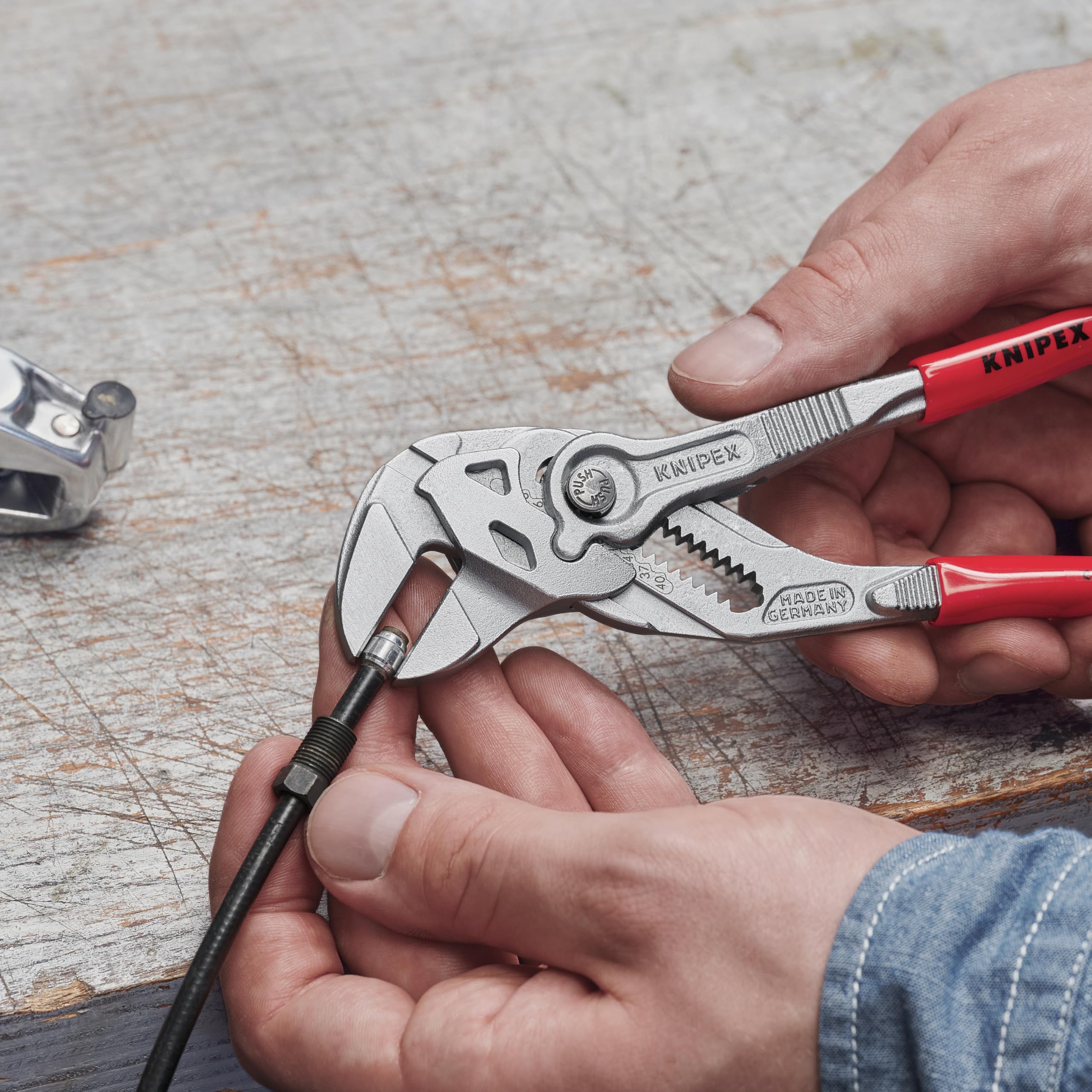 Des mains utilisant une pince-clé KNIPEX aux poignées rouges pour serrer un écrou sur un câble.