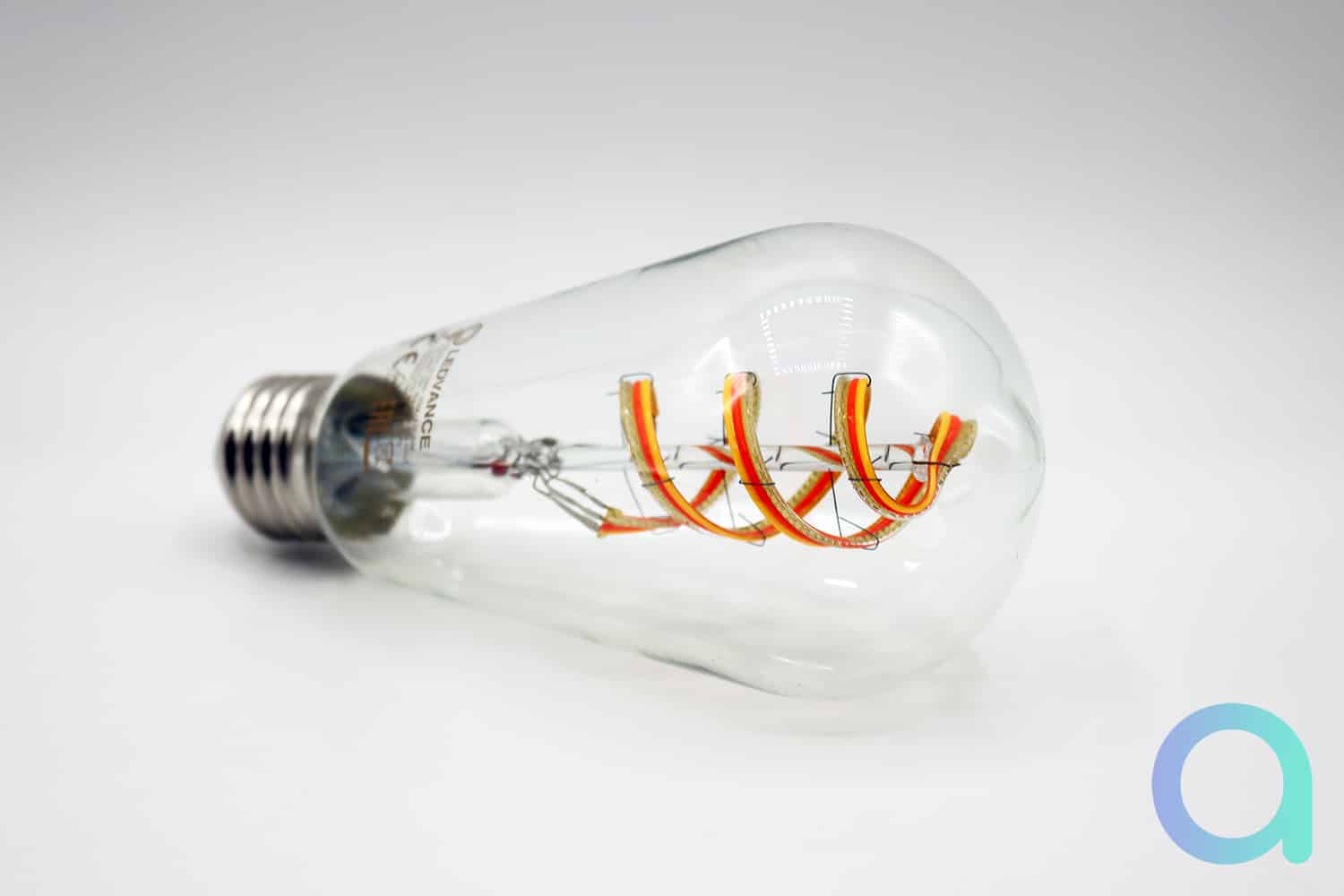Une ampoule LED à filament spiralé de la marque LEDVANCE posée à l’horizontale sur fond blanc.