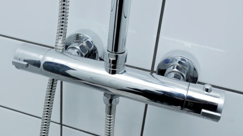 Mitigeur thermostatique chromé installé sur un mur carrelé, avec douchette et flexible de douche visibles