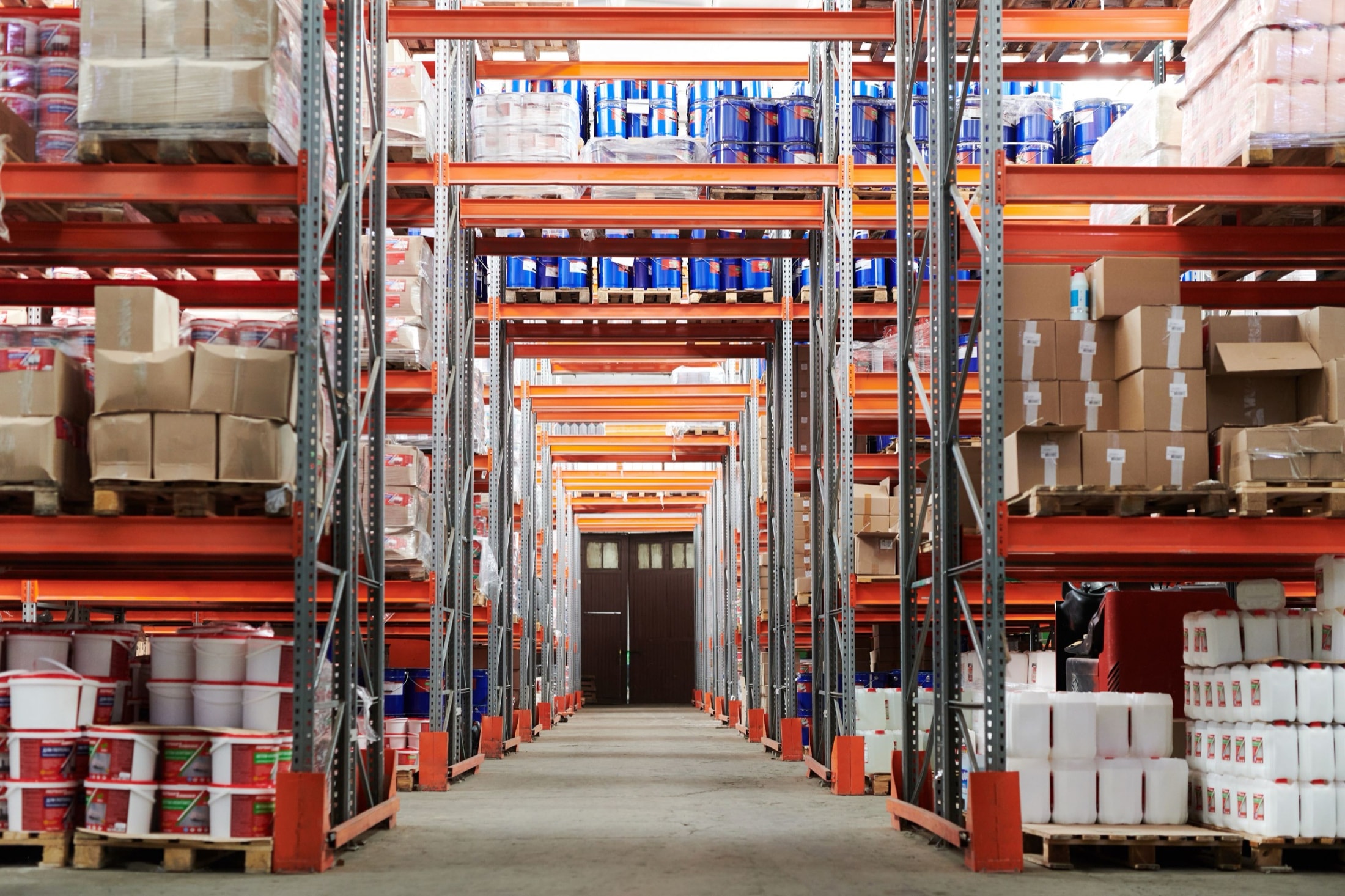 Allée d’un entrepôt logistique bordée de rayonnages industriels chargés de cartons et de palettes