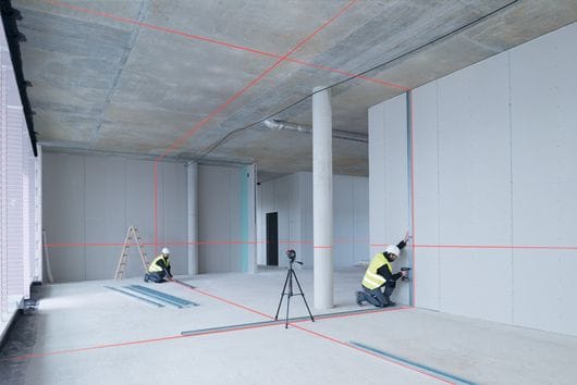 Ouvriers alignant une ossature de cloison à l’aide d’un laser lignes sur trépied