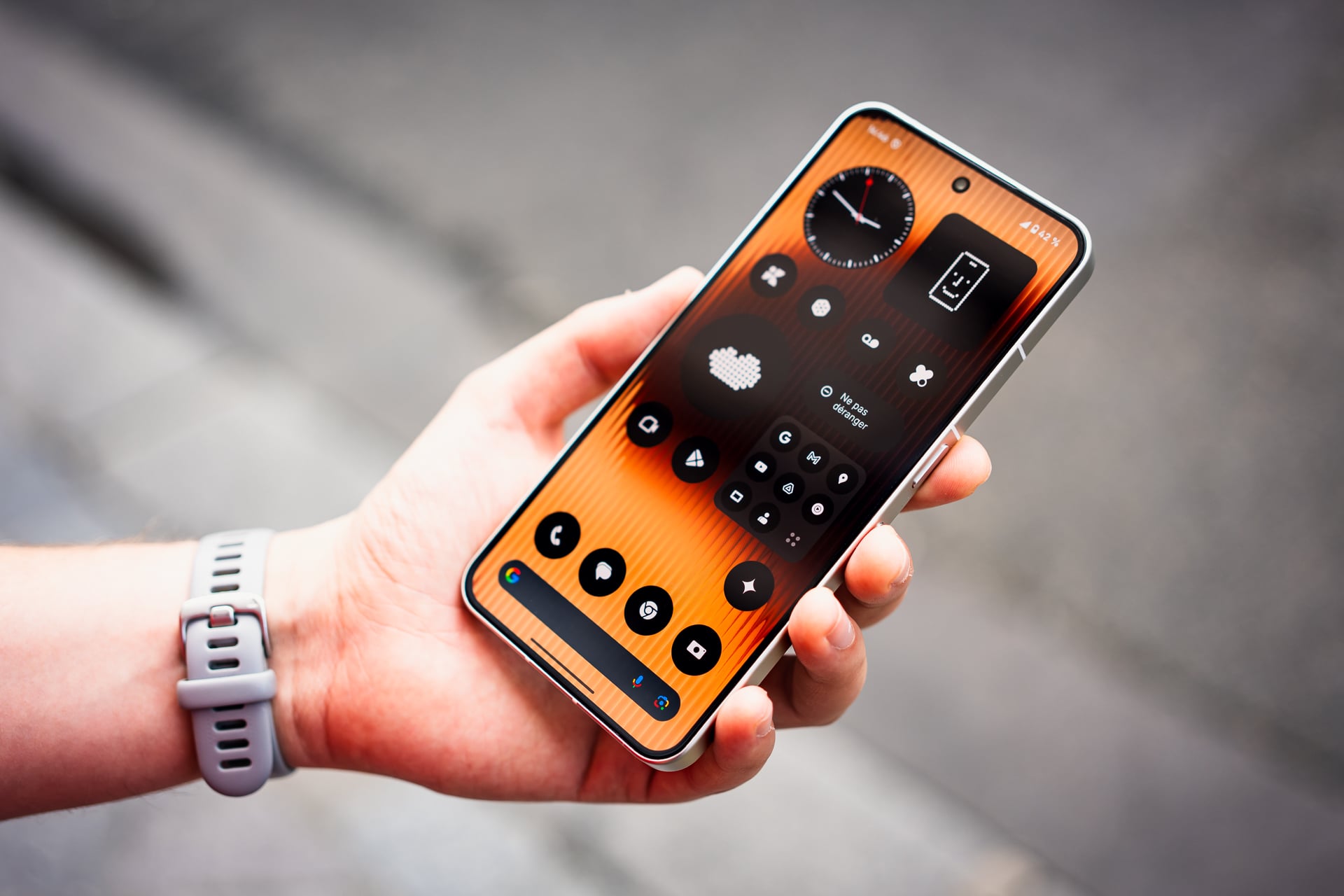 Main tenant un smartphone affichant une interface utilisateur orange avec des icônes noires rondes et une barre de recherche