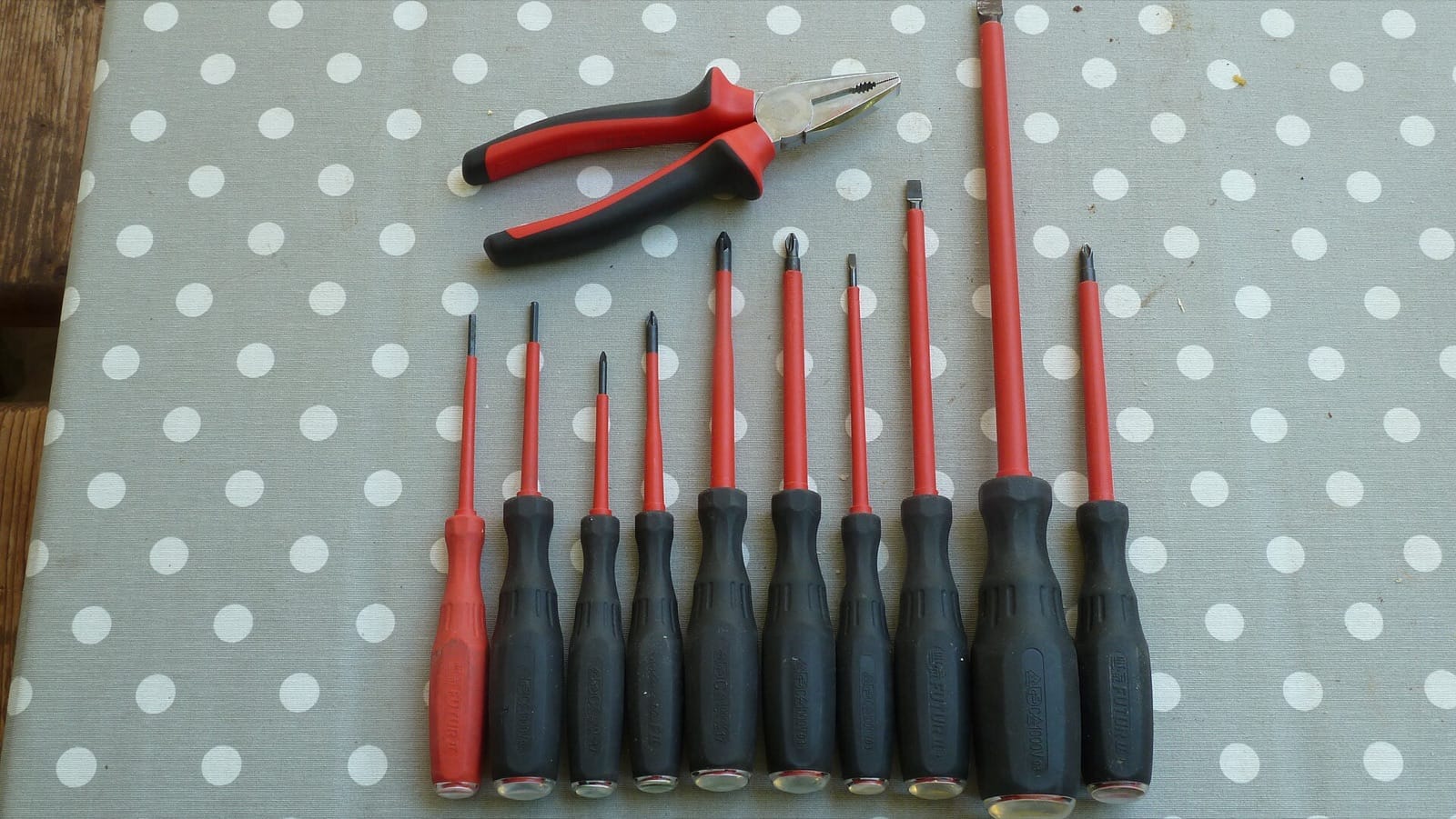 Jeu de tournevis isolés à tiges rouges et pince combinée à poignées noires et rouges disposés sur une table