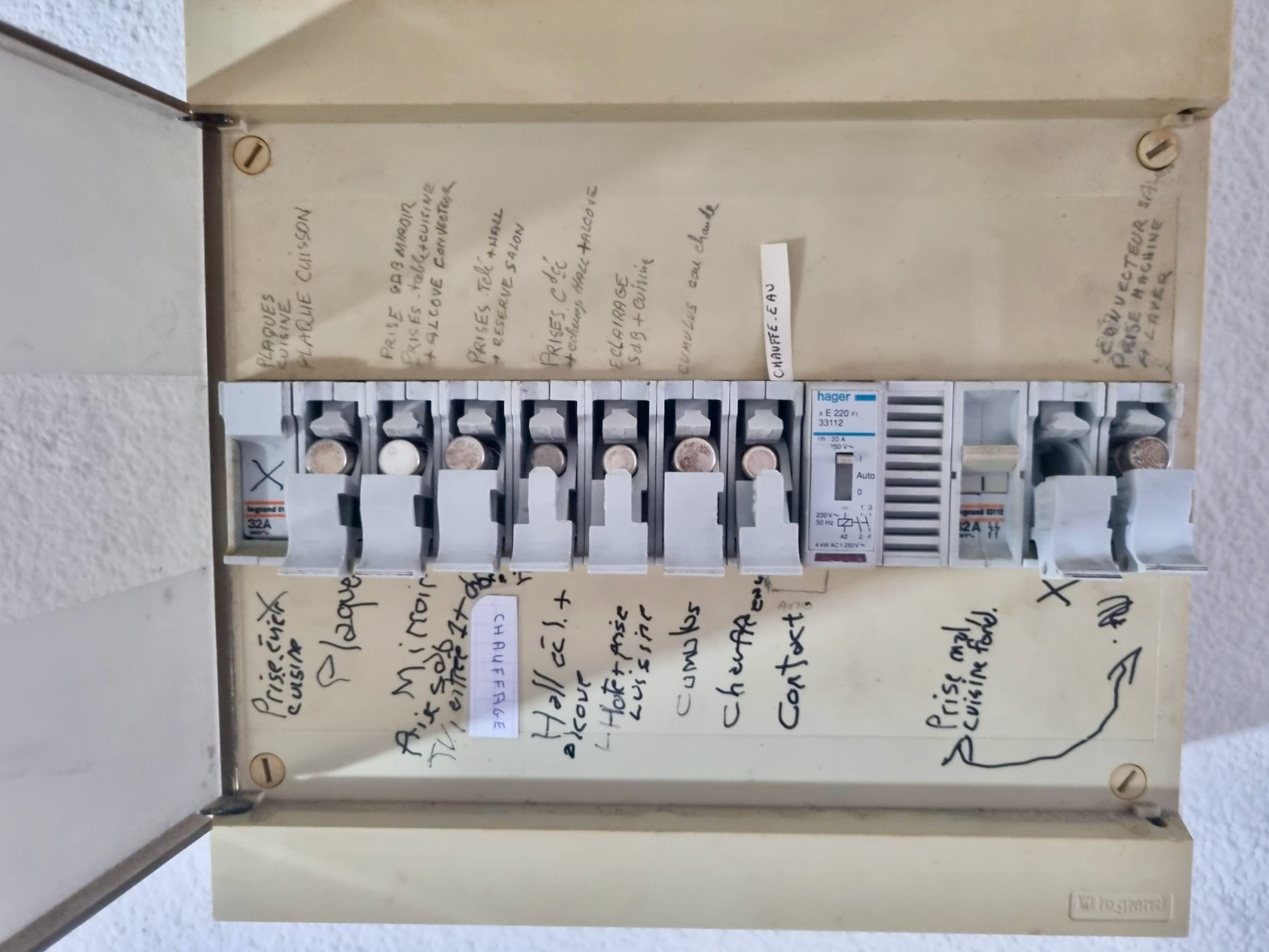 Ancien tableau électrique ouvert avec rangée de fusibles et inscriptions manuscrites des circuits