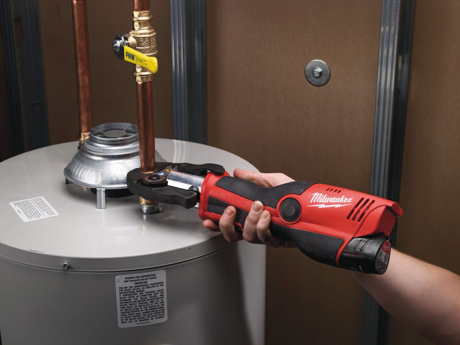 Milwaukee M12 HPT tenue à une main sur un raccord de tube cuivre près d'un chauffe-eau