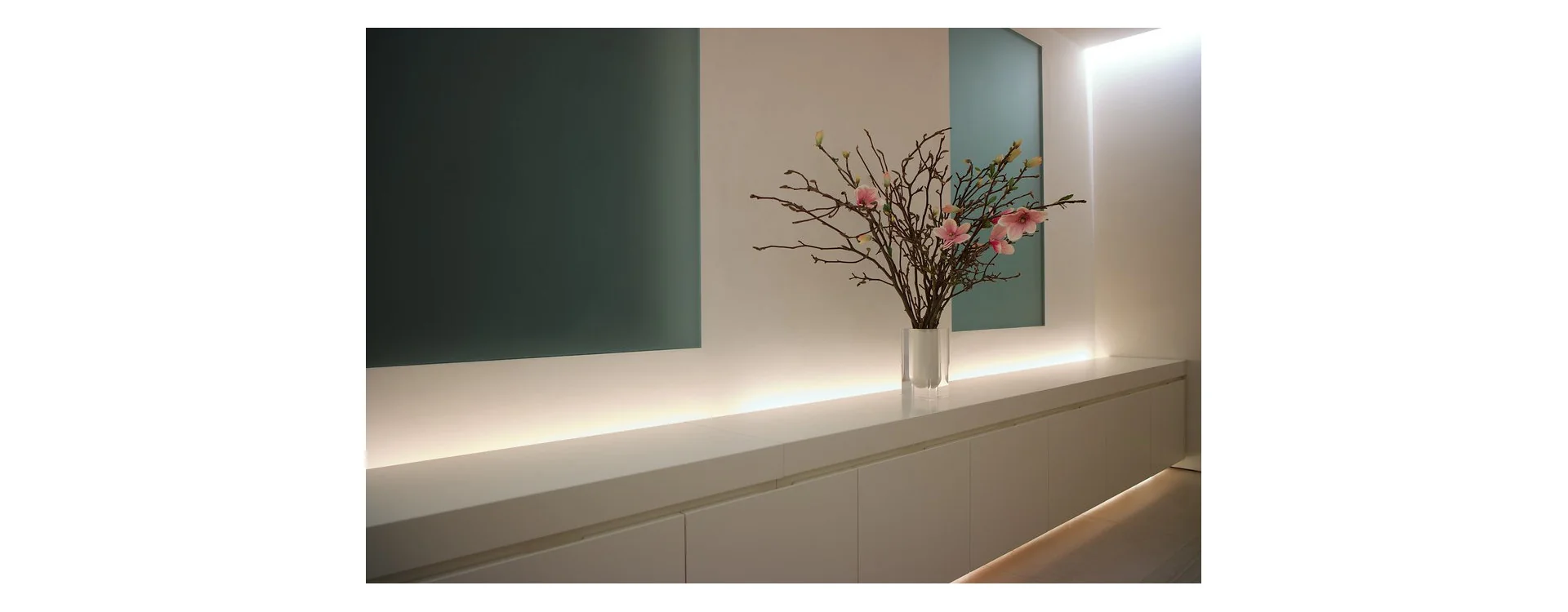 Installation de ruban LED sous un meuble blanc avec un vase contenant des branches fleuries