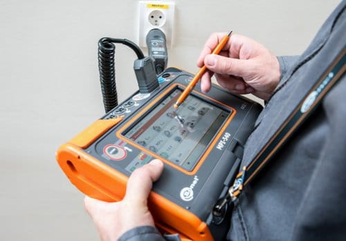 Technicien utilisant un contrôleur Sonel MPI-540 relié à une prise par un adaptateur