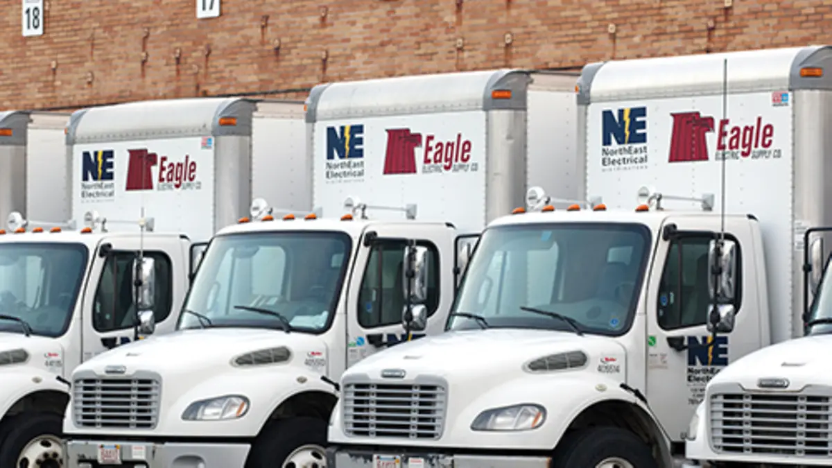 Camions blancs marqués NorthEast Electrical et Eagle Electric Supply alignés devant un entrepôt