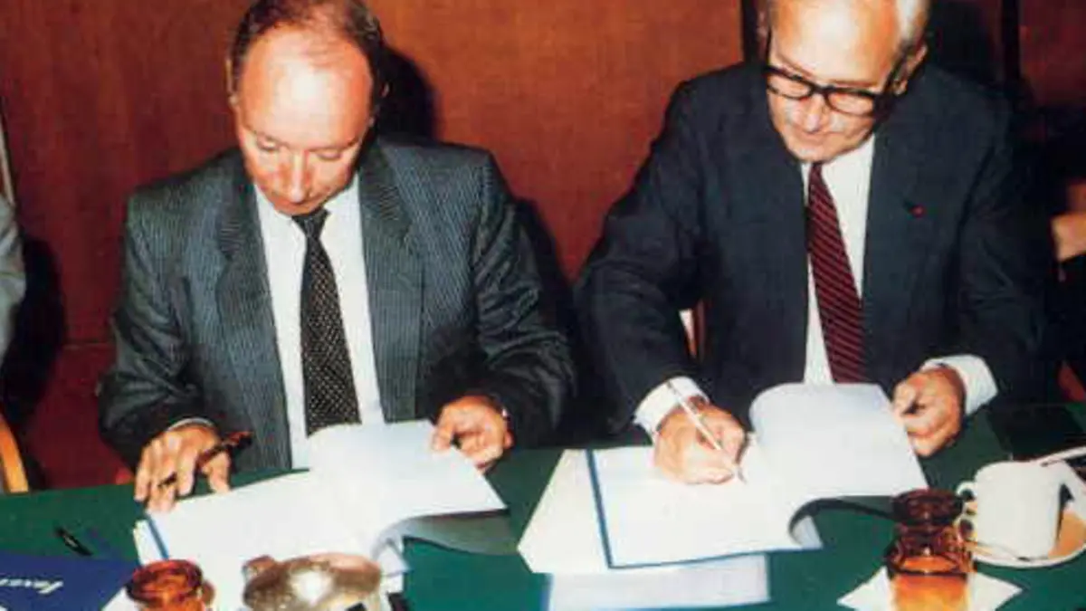 Photographie d’archive de deux personnes signant un document lors de l’acquisition d’Otra