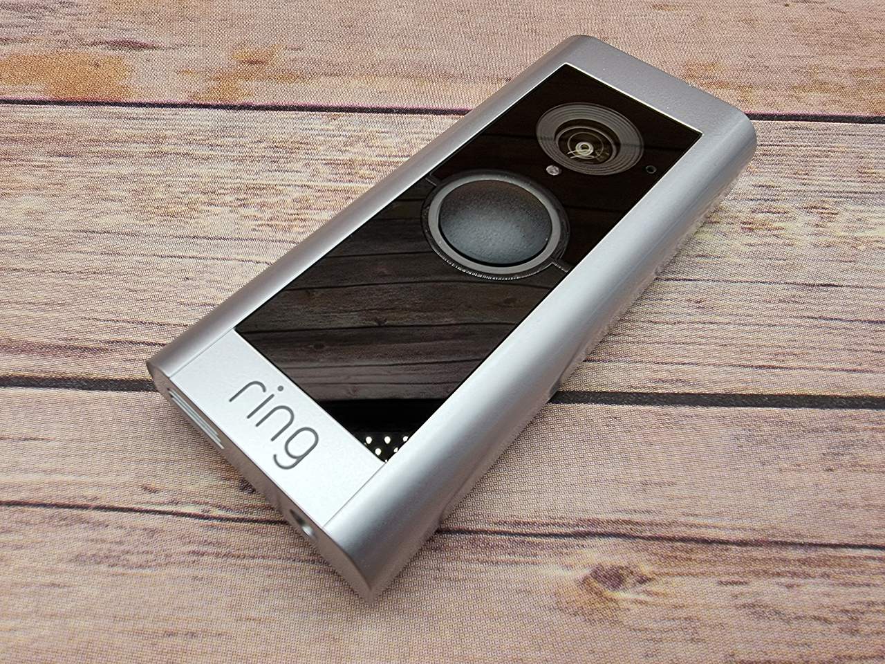 Une sonnette vidéo Ring posée sur une surface en bois montrant son objectif caméra et son bouton avec le logo ring visible