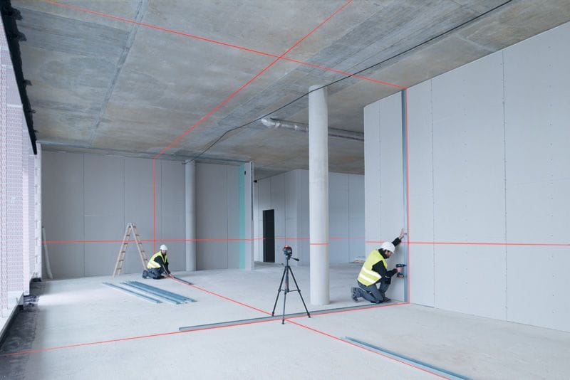 Deux compagnons implantant des rails de cloison avec un laser lignes Bosch sur trépied projetant des lignes rouges au sol, aux murs et au plafond