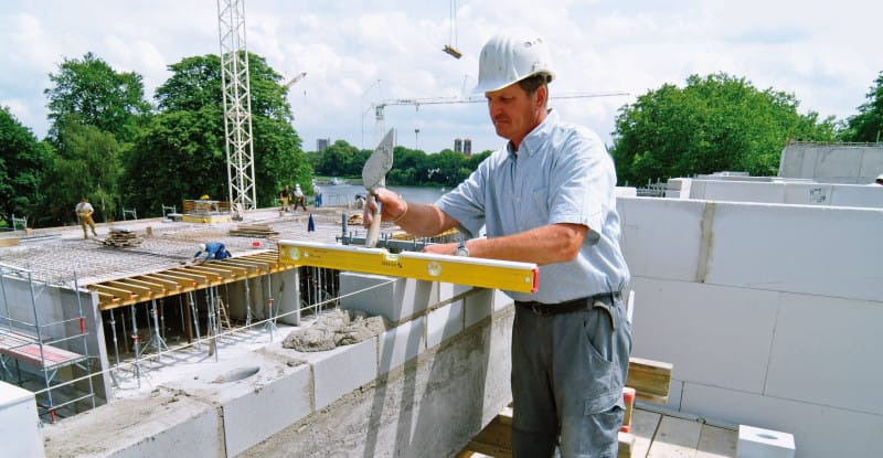 Maçon contrôlant un rang de blocs avec un niveau à bulle STABILA jaune sur un chantier de gros oeuvre