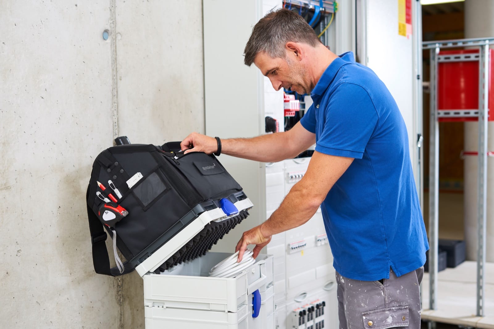 Électricien travaillant sur une armoire ouverte avec une caisse Systainer blanche posée devant lui