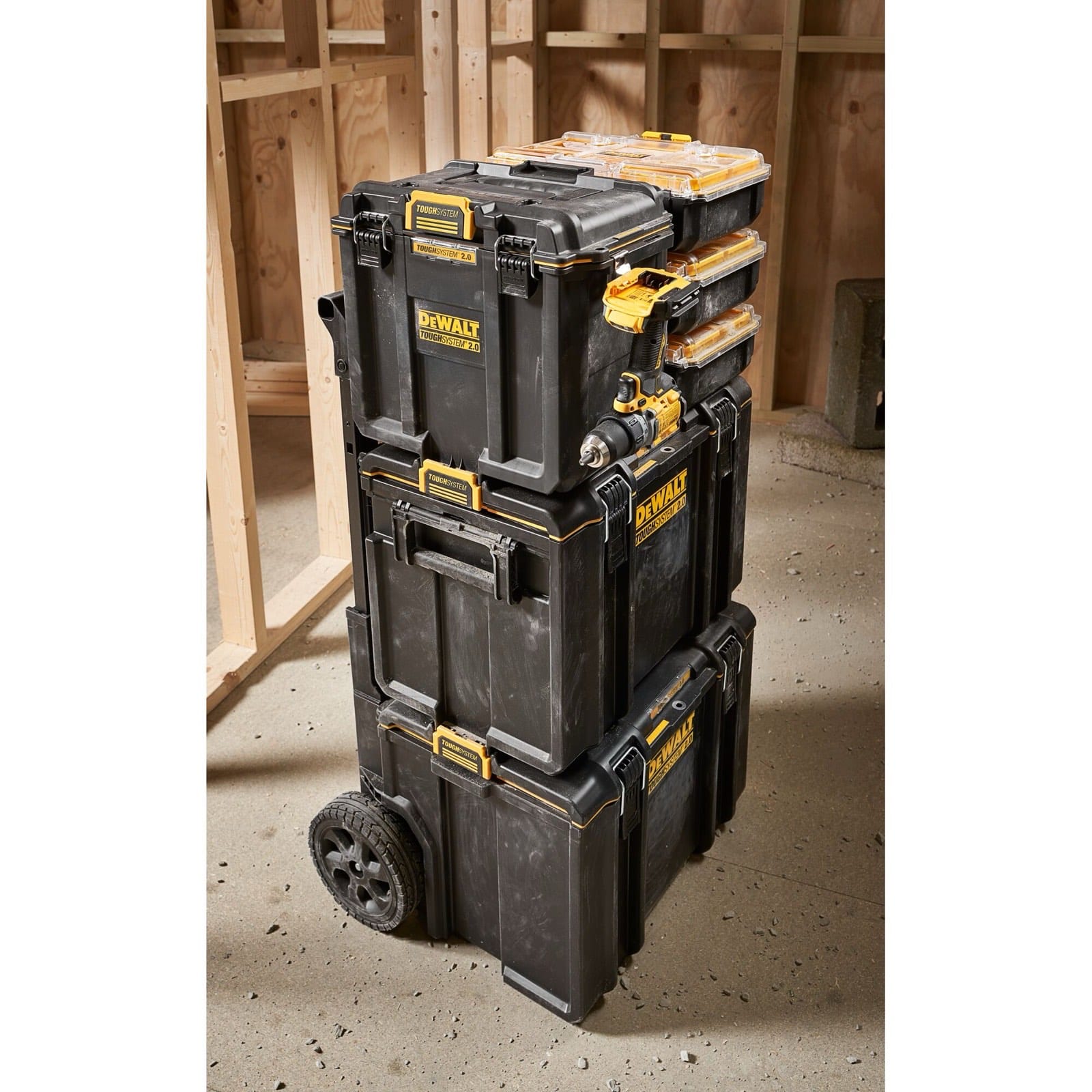 Trois coffrets Dewalt ToughSystem empilés sur un chantier, avec des bois de charpente en arrière-plan