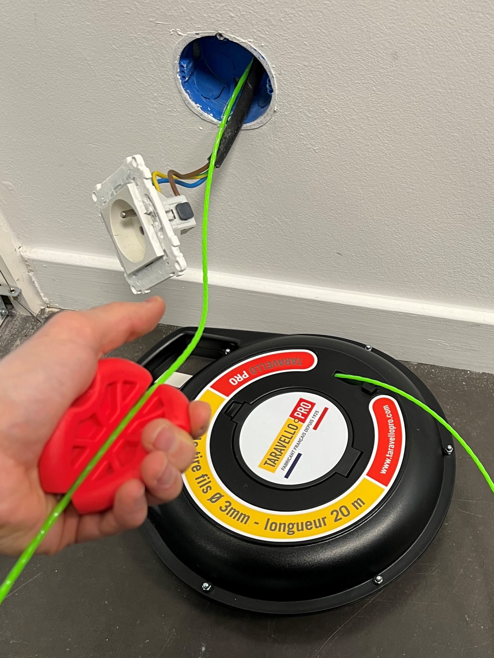 Main tenant l’accessoire rouge fixé au fil vert Taravello Pro sortant d’une boîte d’encastrement