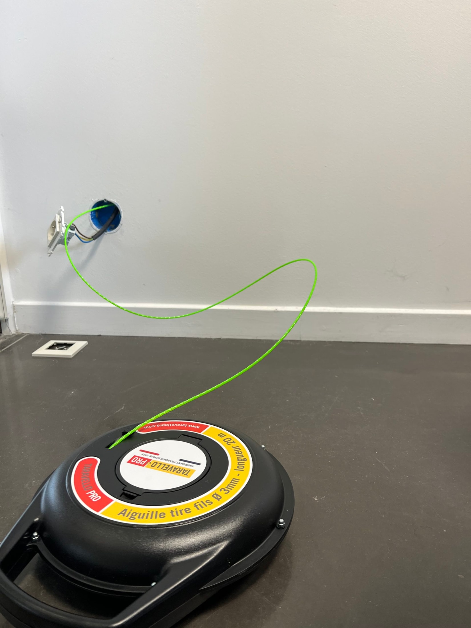 Bobine Taravello Pro posée au sol avec le fil vert déroulé vers une boîte d’encastrement