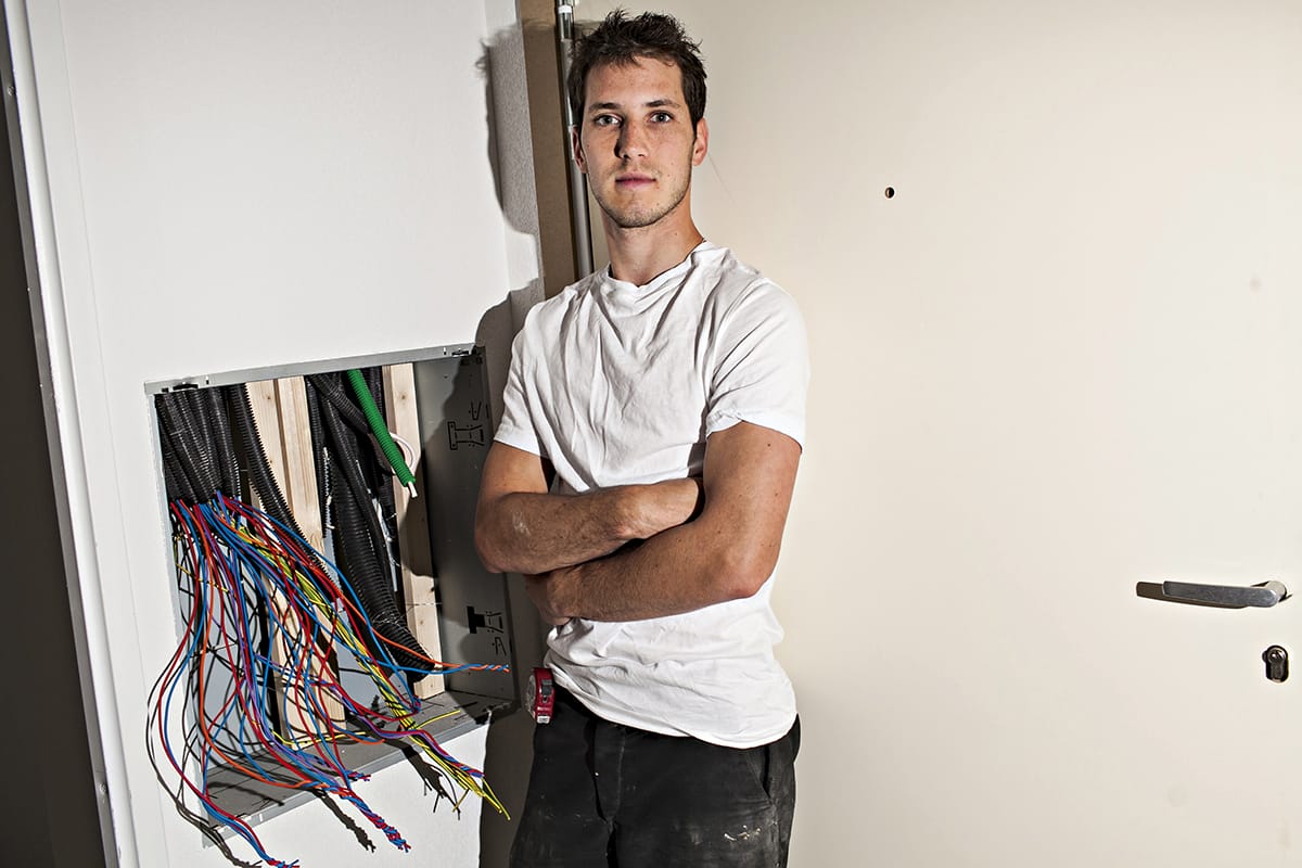 Jeune électricien debout devant un tableau électrique ouvert avec des fils colorés