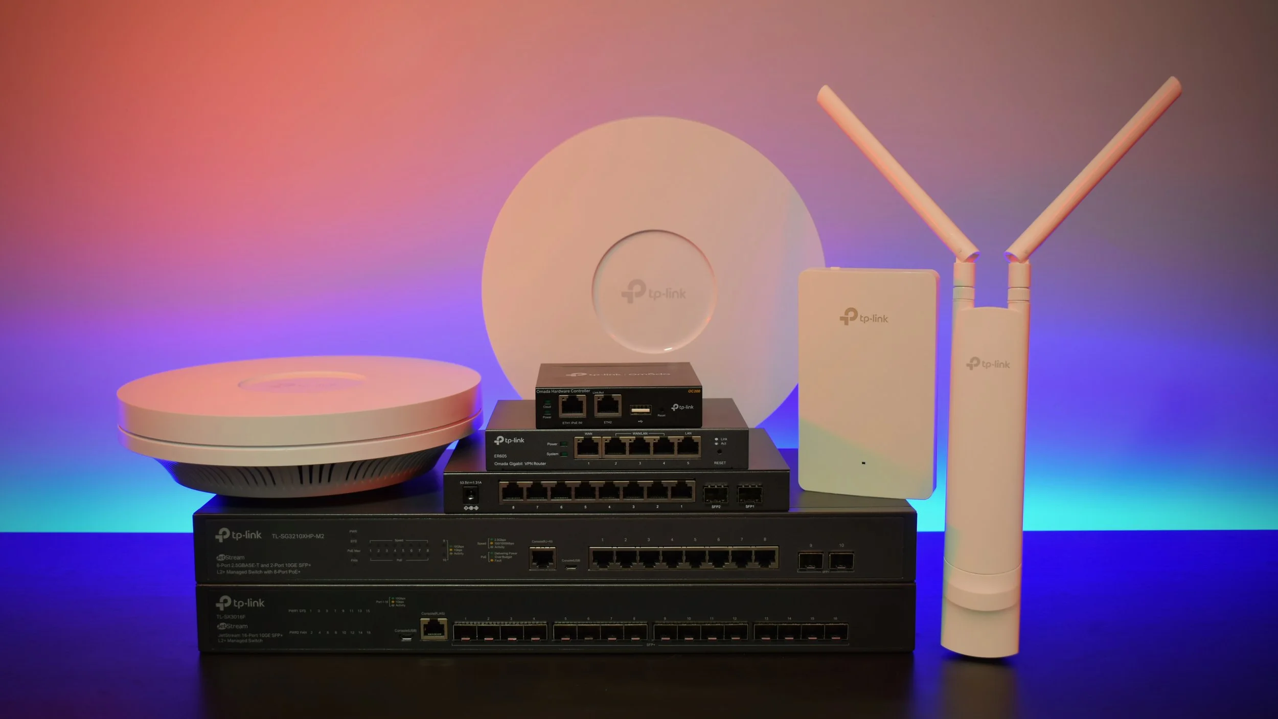 Ensemble d’équipements réseau TP-Link incluant des switches, un routeur, des points d’accès Wi-Fi et une antenne extérieure disposés sur une surface avec un éclairage coloré en arrière-plan.