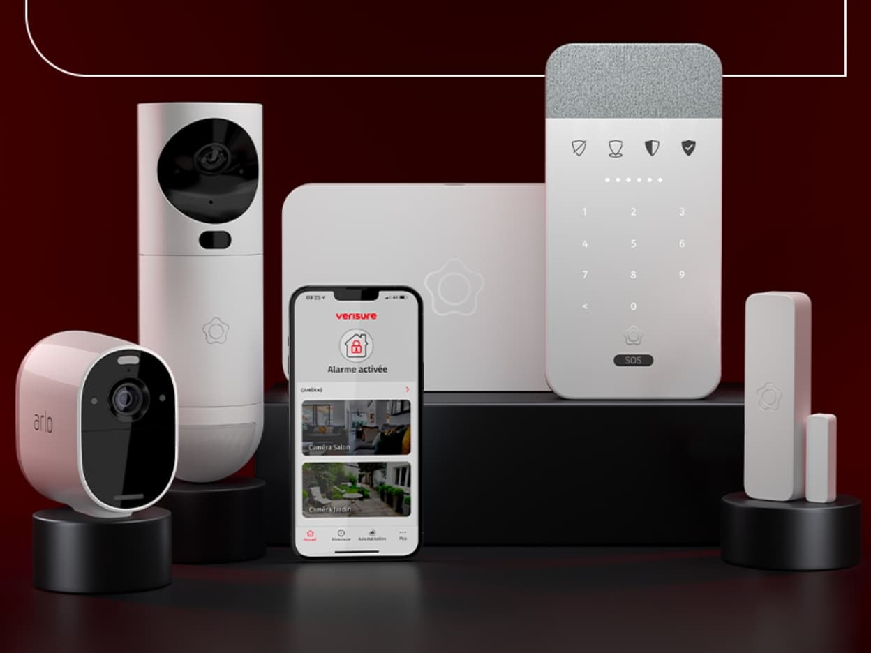 Ensemble d’appareils de sécurité blancs dont une caméra marquée Arlo, disposés sur des socles noirs avec un smartphone affichant l’application Verisure indiquant Alarme activée.
