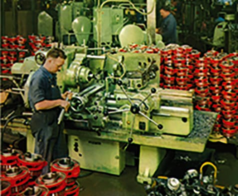 Ouvrier à un tour dans un atelier Virax entouré de filières peintes en rouge