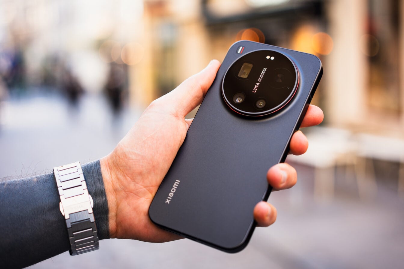 Une main tenant un smartphone noir Xiaomi avec un grand module photo circulaire Leica, avec une montre au poignet.