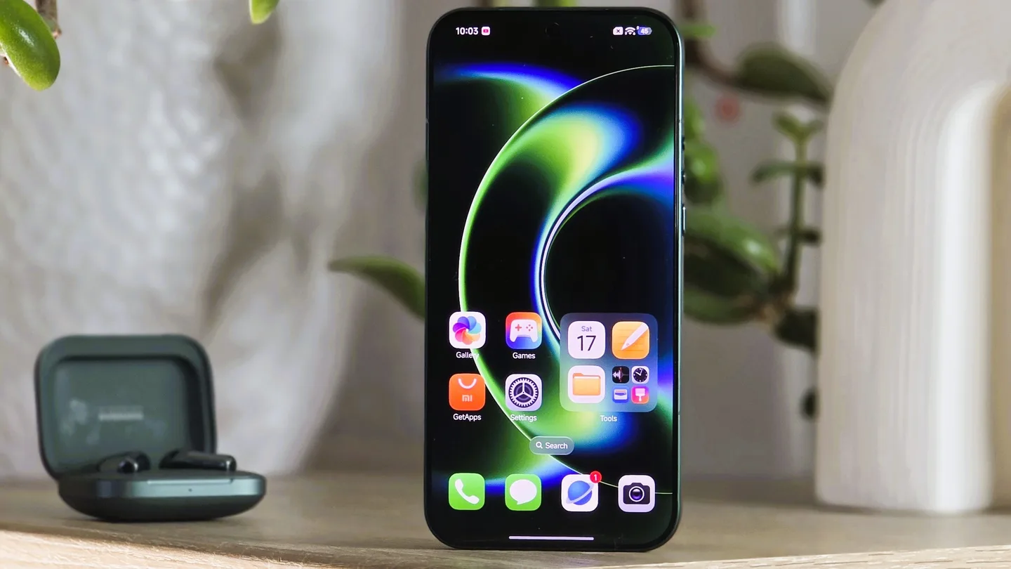 Un smartphone posé sur une table avec l’écran allumé montrant l’interface utilisateur et des icônes d’applications, à côté d’un boîtier d’écouteurs ouvert.