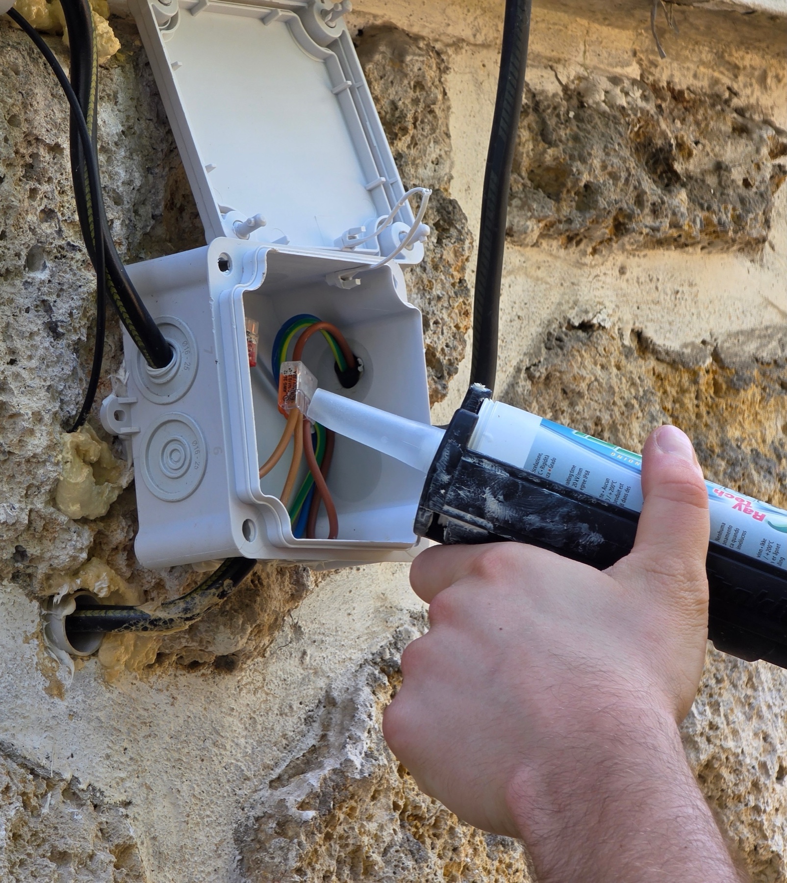 Application du gel isolant Raytech sur une boîte de dérivation extérieure fixée sur un mur en pierre, avec connecteurs Wago