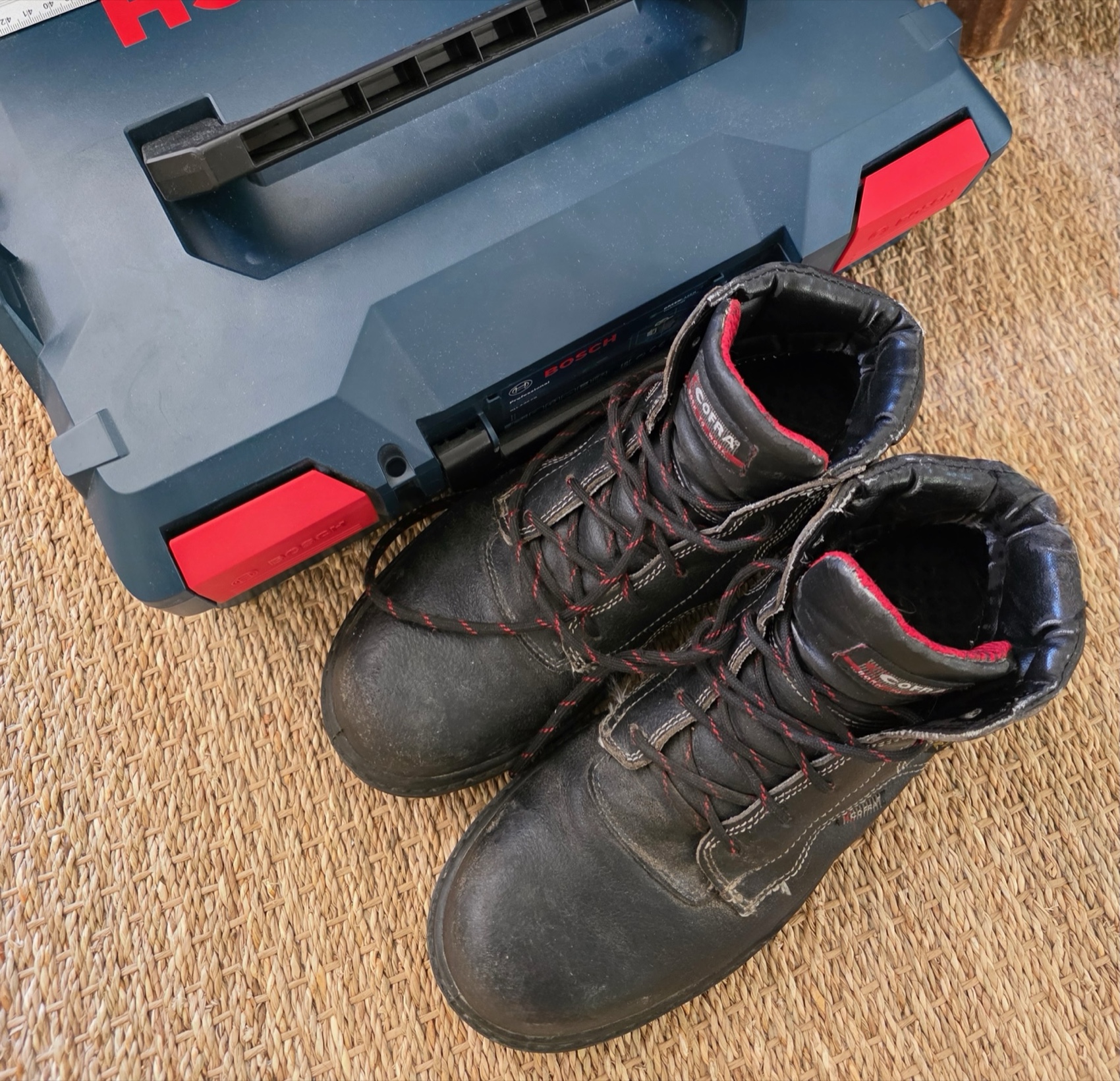 Bottes de sécurité Cofra noires à lacets rouges posées devant une caisse à outils Bosch L-Boxx