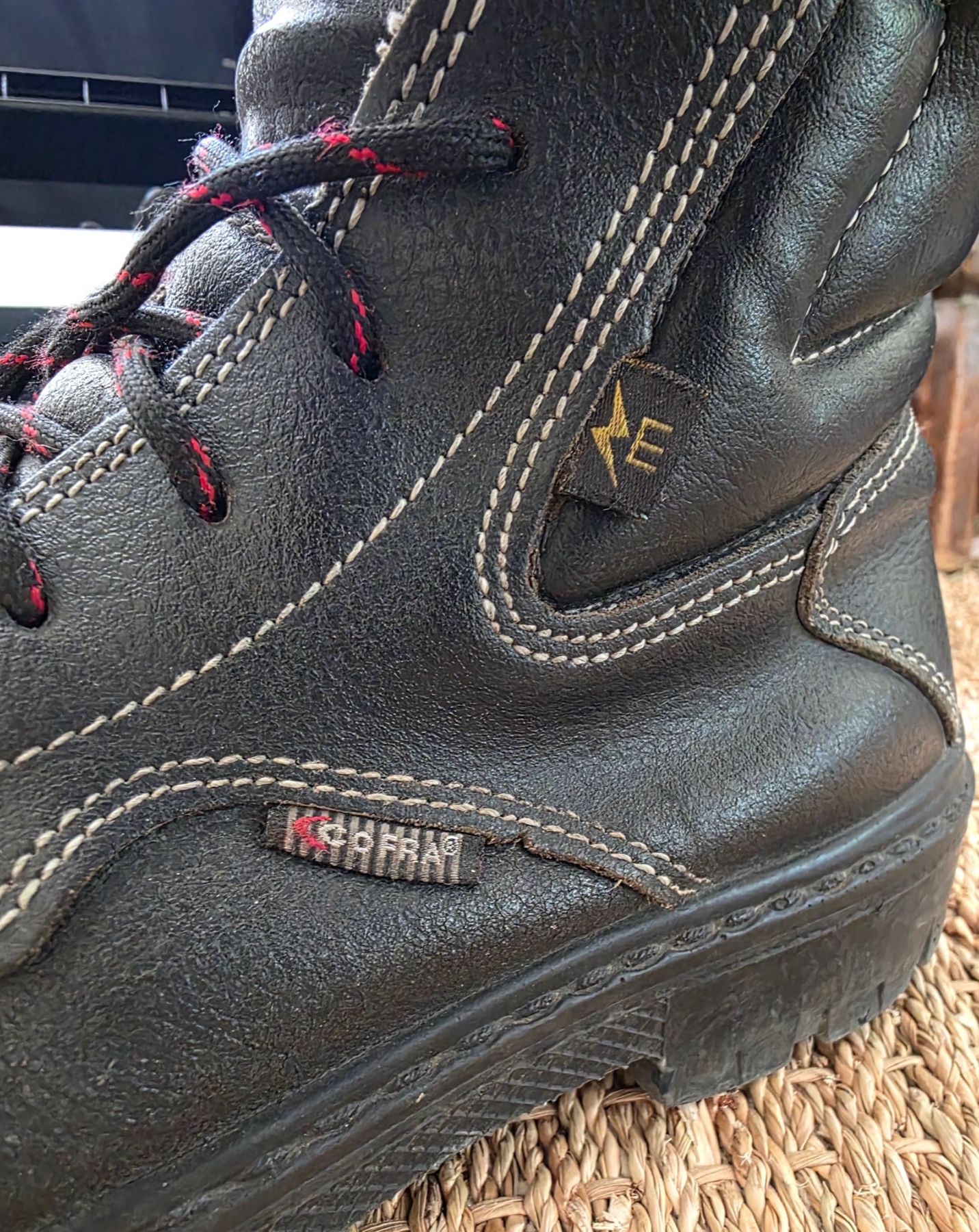 Côté d’une botte de sécurité Cofra noire avec couture blanche et logo E électrique près de la semelle