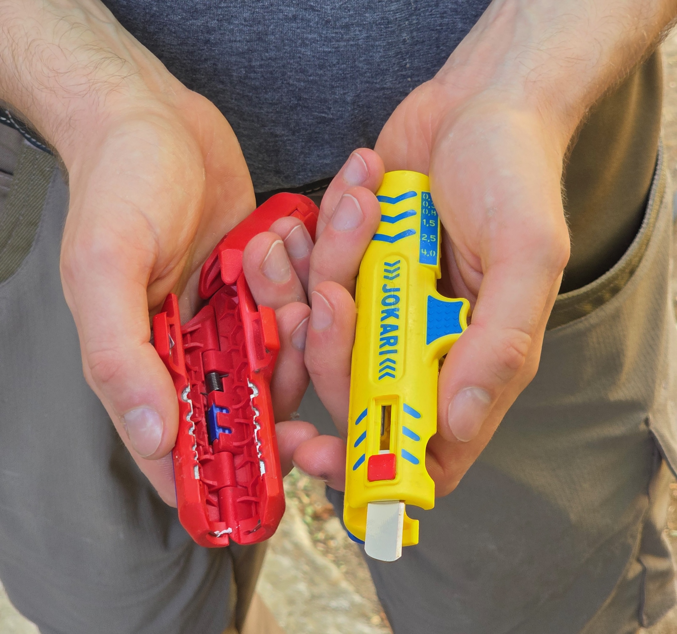 Un dénudeur jaune Jokari et un dénudeur rouge ouvert, tenus dans les mains d’un électricien