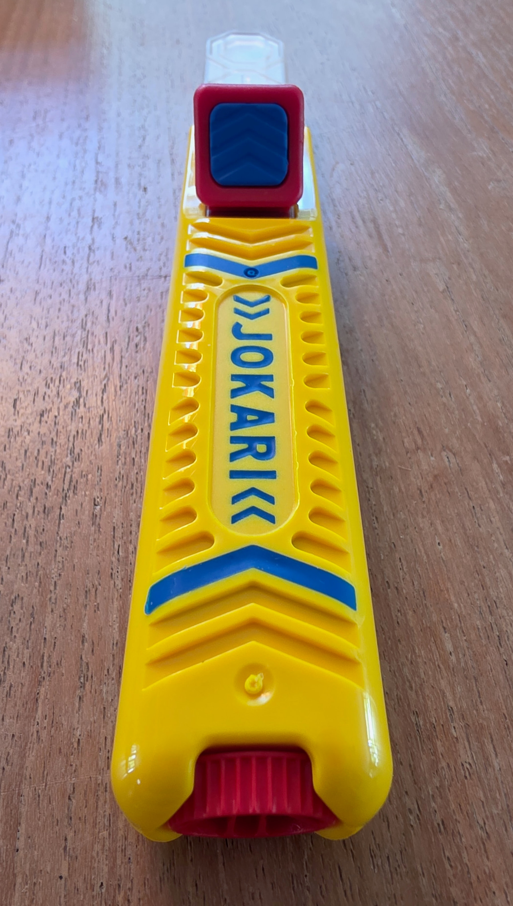 Pince à dénuder Jokari jaune avec inscription bleue et bouton rouge, vue de dessus