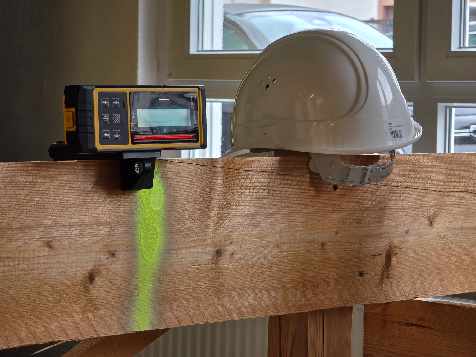 Récepteur laser STABILA fixé sur une poutre en bois avec un trait laser vert projeté et un casque de chantier blanc